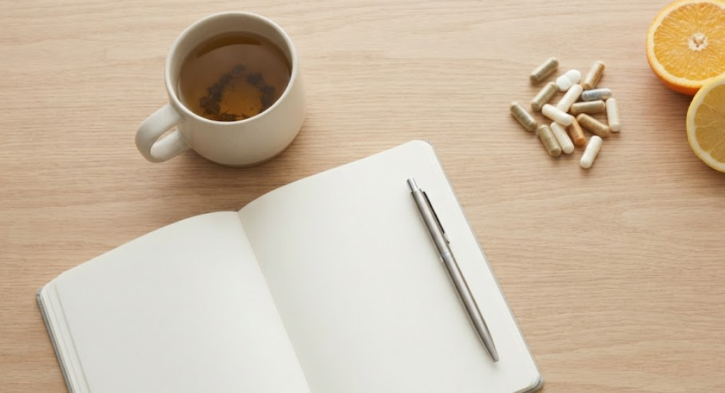 minimalist flat lay on wood table with herbal tea, journal, supplements, and citrus