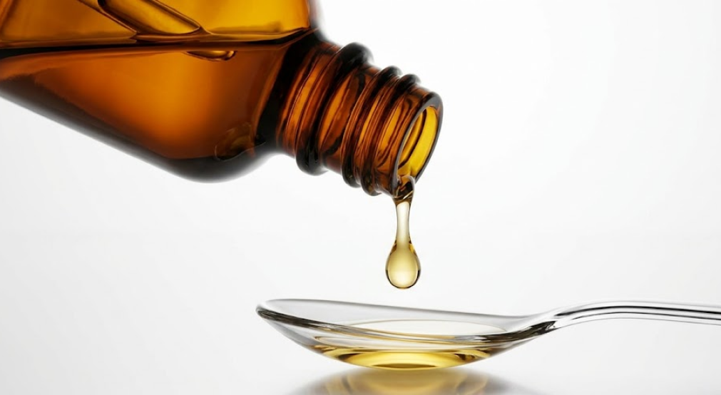 Amber glass dropper bottle dispensing a golden liquid nutrient drop onto a clear spoon