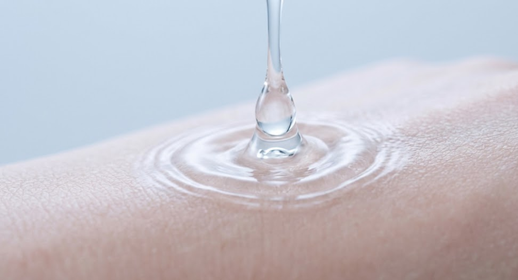 A high-speed macro photograph capturing a clear liquid droplet splashing gently onto smooth skin.
