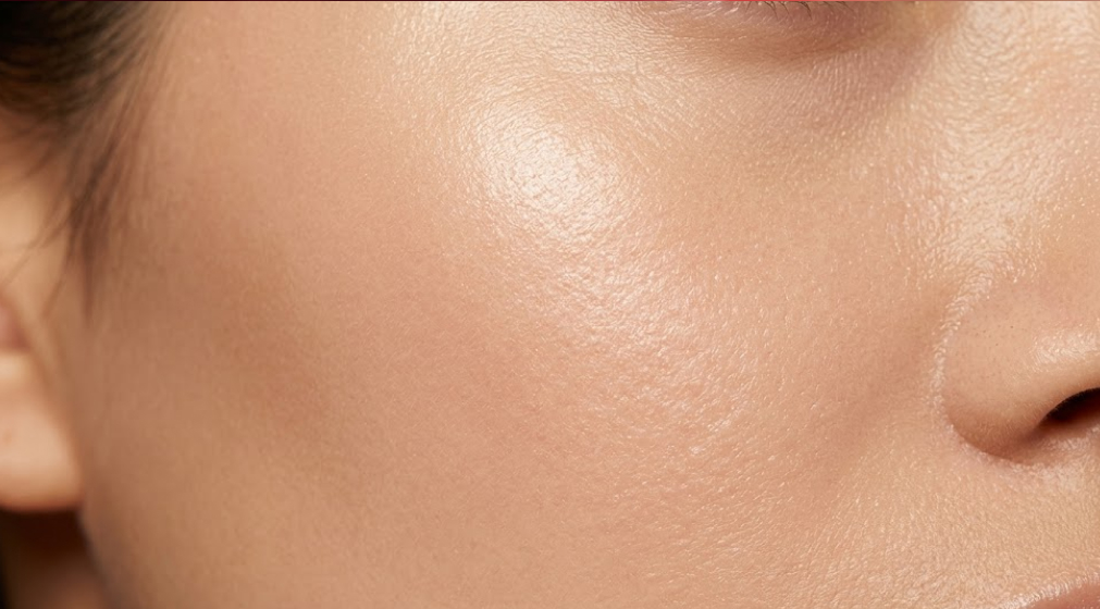 A close-up view of radiant, smooth human cheek skin with invisible pores and a healthy moisture sheen.